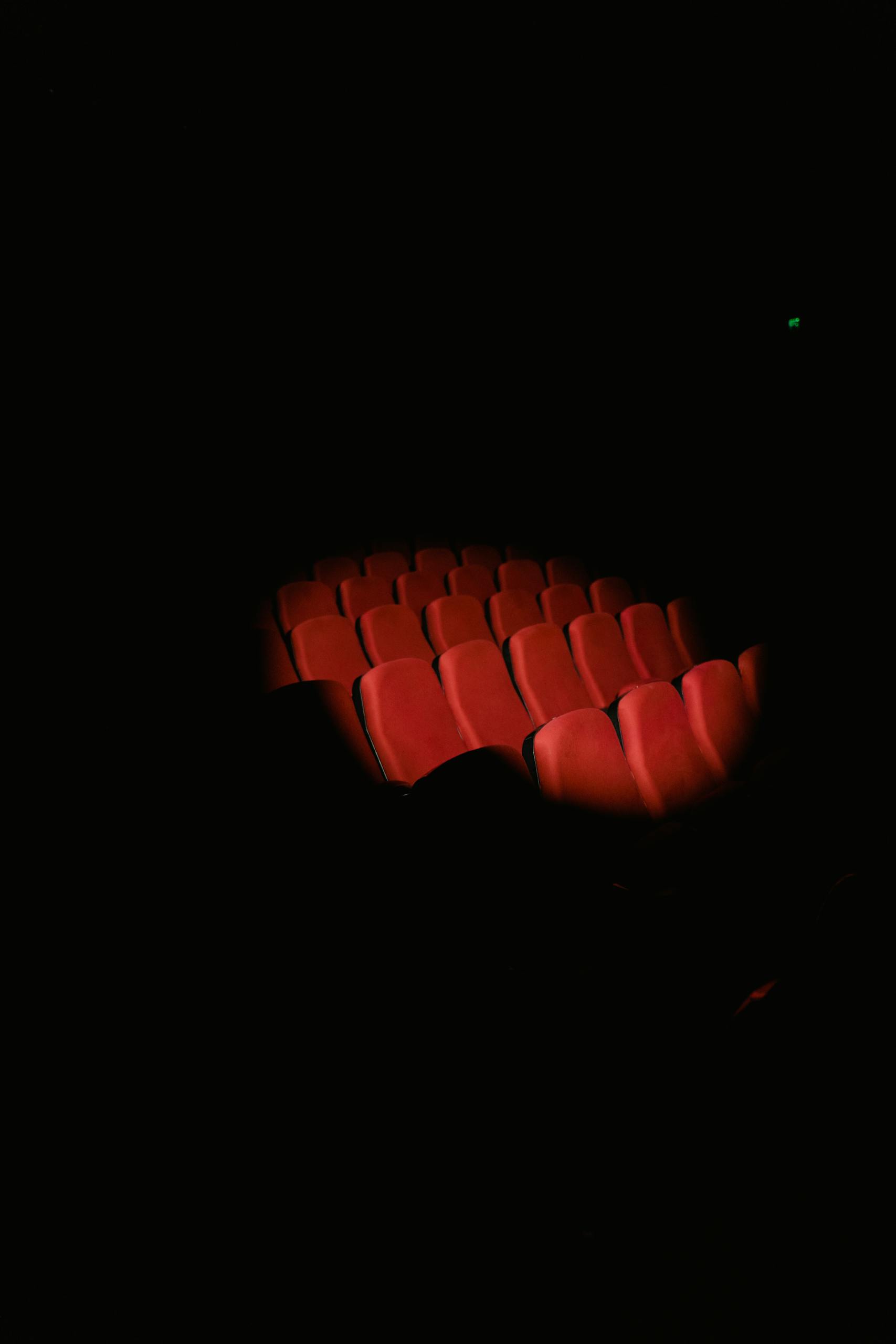 Rows of red theater seats illuminated by a spotlight in a dark cinema.